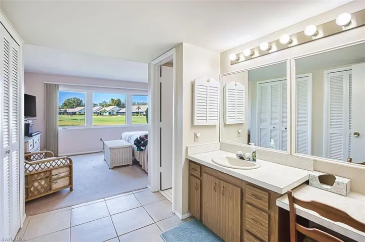 Ensuite bathroom featuring a closet, vanity, light colored carpet, light tile patterned flooring, and a residential view