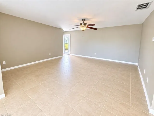 Spacious room featuring neutral tone walls, tile flooring, and a ceiling fan with integrated lighting
