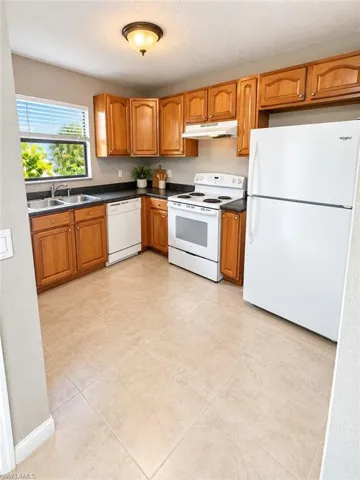 Kitchen featuring light wood cabinetry, black countertops, and a full suite of white appliances