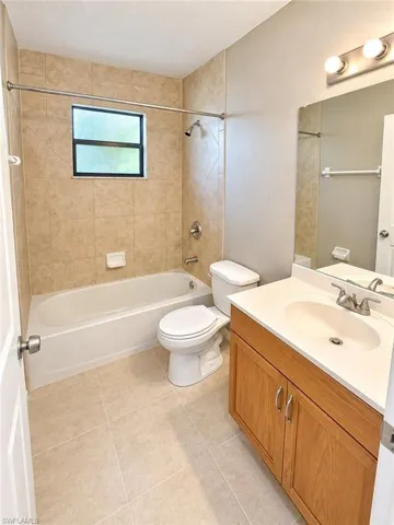 Tub and shower combination with tiled surround, light wood-finish vanity with integrated sink, and tiled flooring