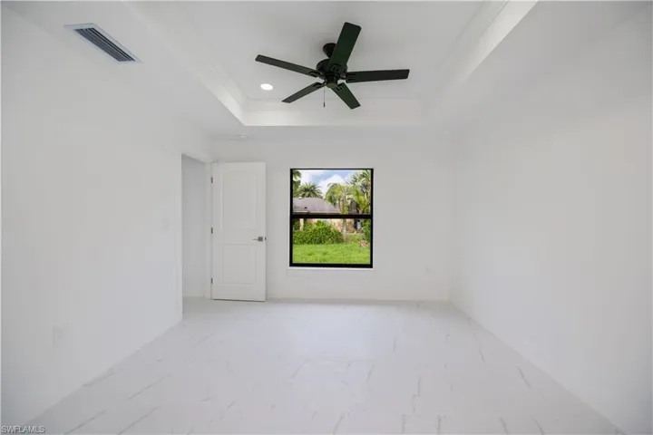 Empty room with light marble finish flooring, ornamental molding, a tray ceiling, ceiling fan, and recessed lighting
