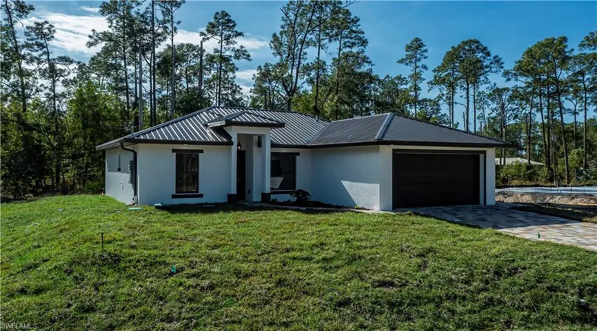 View of front of home featuring stucco siding, decorative driveway, a garage, and a metal roof