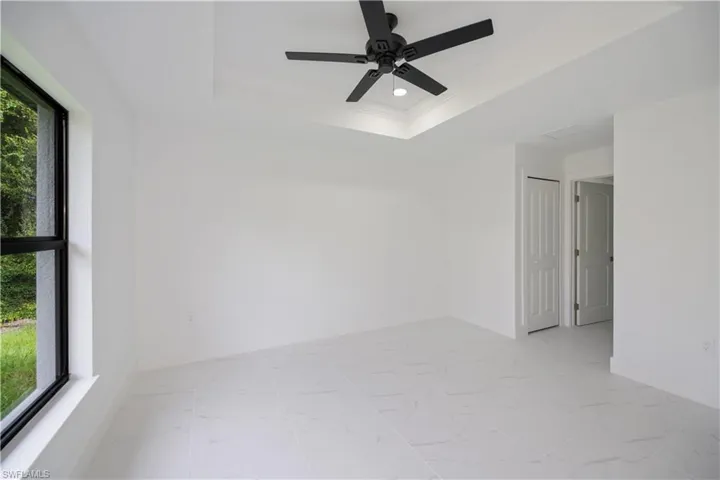 Spare room with a raised ceiling, light marble finish floors, ornamental molding, recessed lighting, and ceiling fan