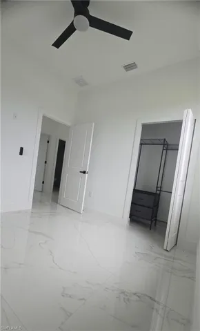Spacious room with large-format marble-look tile flooring, crisp white walls, and a contemporary black ceiling fan