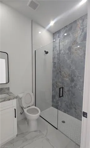 Walk-in shower featuring gray veined wall tiles, a hexagon tile floor, and a black-framed glass enclosure