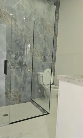 Glass-enclosed shower featuring large format tile surround with natural stone appearance and hexagonal mosaic floor