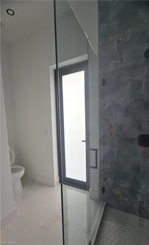 Modern bathroom featuring a frameless glass shower enclosure with matte black hardware, large format marble-look floor tiles, dark-toned shower wall tiling, and a black-framed privacy door