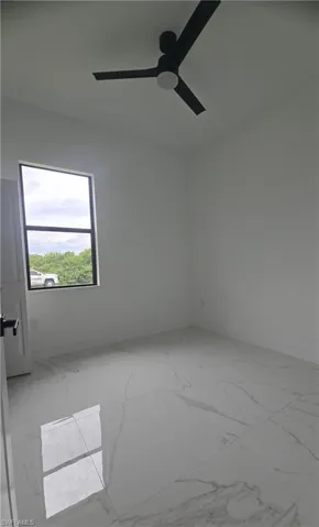 Room featuring white walls, large format tile flooring, a dark-framed window, and a ceiling fan with integrated lighting
