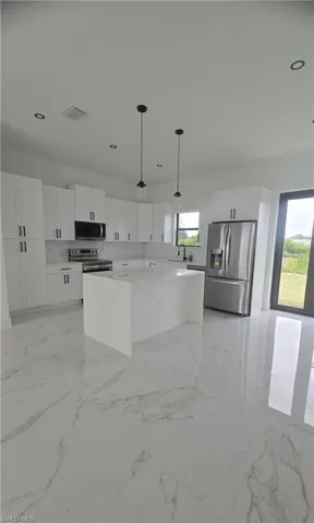 Modern kitchen featuring a large center island with a solid surface countertop, white shaker cabinetry, and stainless steel appliances