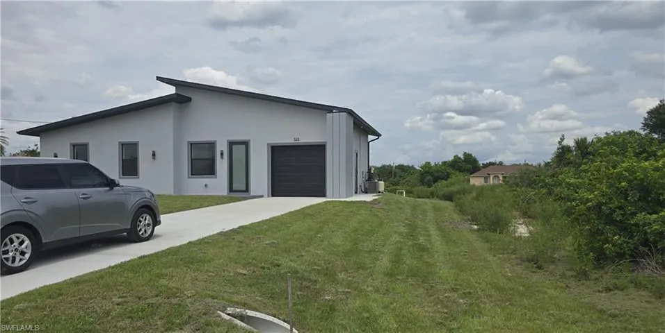 Contemporary grey stucco exterior featuring a dark grey garage door, a modern entry door with a vertical glass panel, and exterior wall sconces