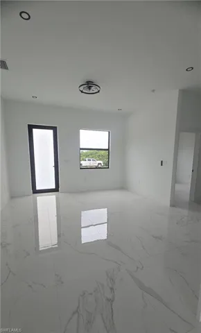 Spacious room featuring polished white tile flooring with gray veining, a black-framed glass-paneled door, and recessed lighting