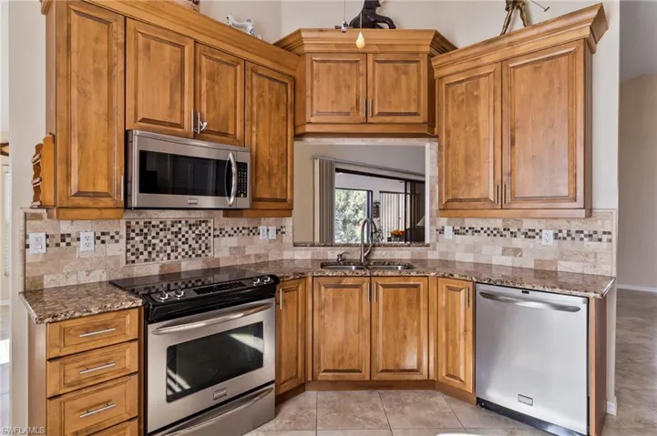 Kitchen with light tile patterned flooring, appliances with stainless steel finishes, tasteful backsplash, sink, and granite counters