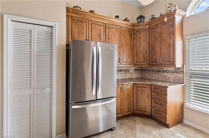 Kitchen with light tile patterned floors, pantry, decorative backsplash, stainless steel fridge, and granite countertops