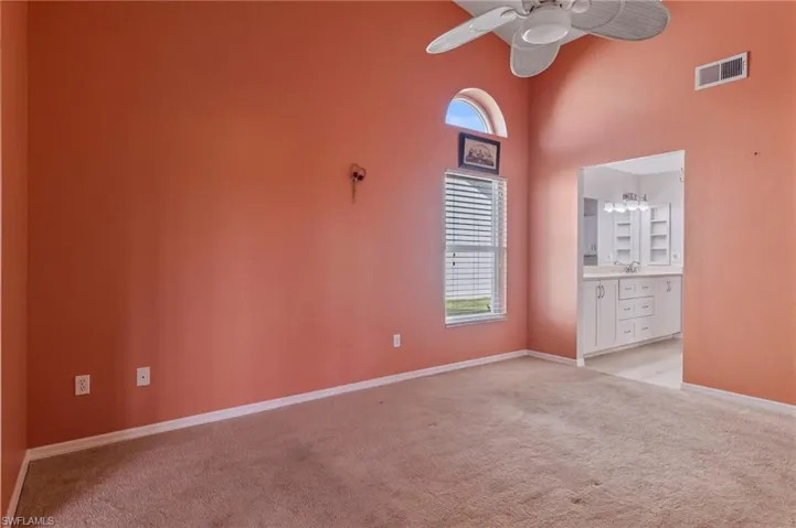 Primary bedroom featuring light carpet,  ceiling fan, and a high ceiling