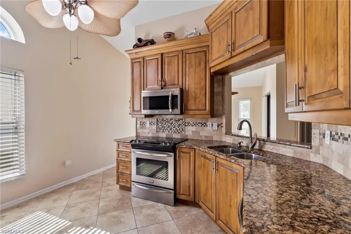 Kitchen with light tile patterned flooring, sink, dark stone countertops, stainless steel appliances, and backsplash