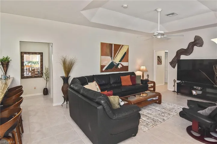 Living area featuring a tray ceiling, light tile patterned floors, and ceiling fan