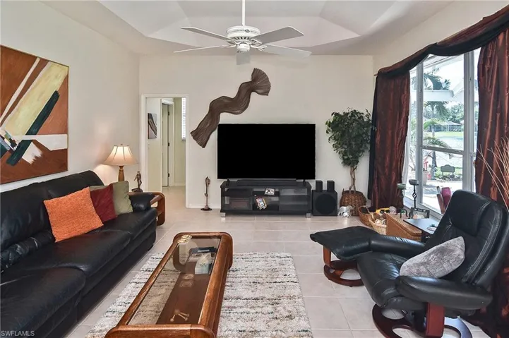 Living area featuring light tile patterned floors, a tray ceiling, and a ceiling fan