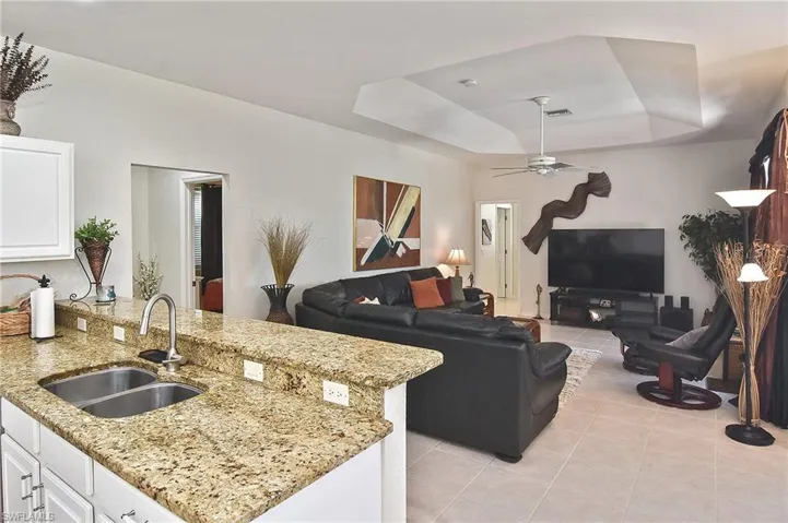 Kitchen with a raised ceiling, light tile patterned floors, light stone countertops, white cabinetry, and a ceiling fan