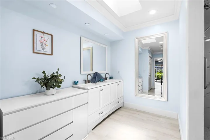 Full bathroom with ornamental molding, light wood-style floors, double vanity, a skylight, and recessed lighting