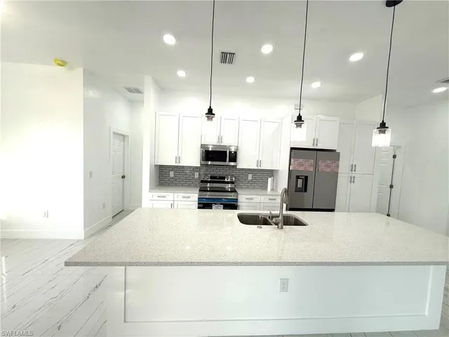 Kitchen with appliances with stainless steel finishes, backsplash, white cabinets, light stone countertops, and recessed lighting