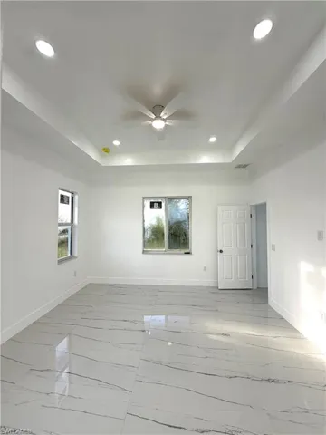 Unfurnished room with a raised ceiling, recessed lighting, light marble finish floors, and ceiling fan