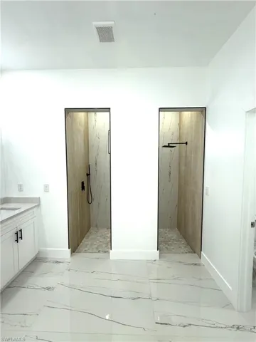 Bathroom with vanity, a marble finish shower, and light marble finish floors