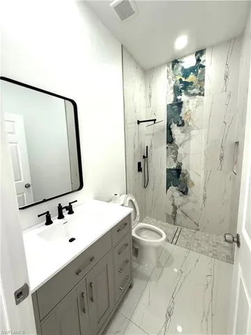 Full bathroom featuring light marble finish flooring, vanity, and a marble finish shower