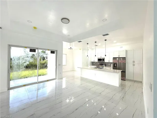Kitchen with hanging light fixtures, white cabinetry, open floor plan, appliances with stainless steel finishes, and a spacious island