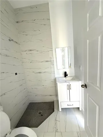 Full bath featuring a marble finish shower, vanity, and light marble finish floors