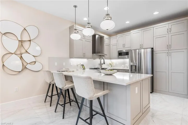 Kitchen with wall chimney exhaust hood, stainless steel appliances, kitchen peninsula, pendant lighting, and a breakfast bar area