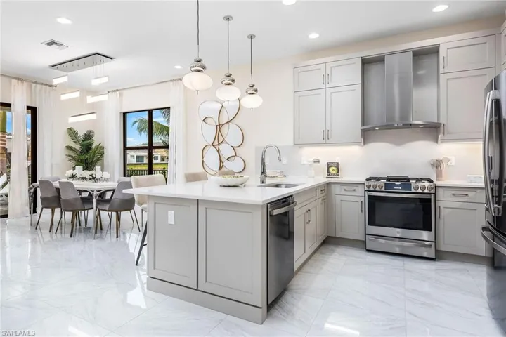 Kitchen featuring gray cabinetry, sink, stainless steel appliances, wall chimney range hood, and decorative light fixtures