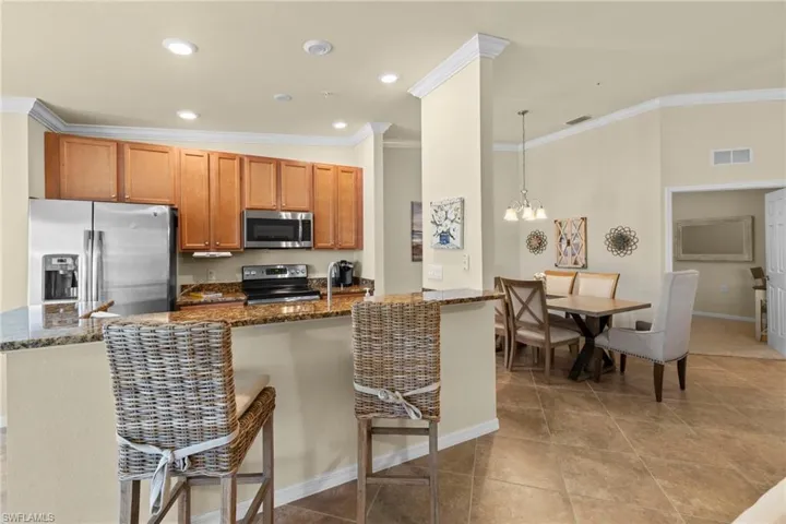 Kitchen featuring visible vents, ornamental molding, dark stone counters, appliances with stainless steel finishes, and a breakfast bar area