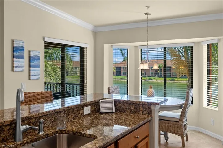 Kitchen featuring crown molding, light tile patterned floors, dark stone countertops, hanging light fixtures, and a sink