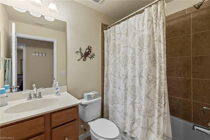 Bathroom featuring visible vents, shower / bath combo with shower curtain, toilet, vanity, and a textured wall