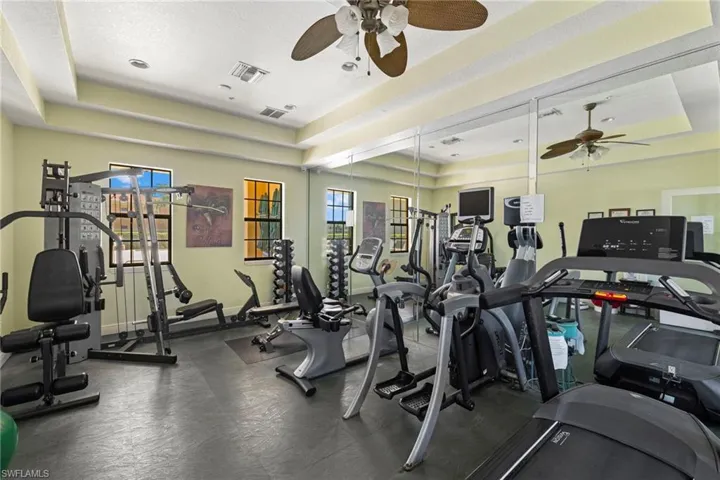 Workout area with a tray ceiling, visible vents, and ceiling fan