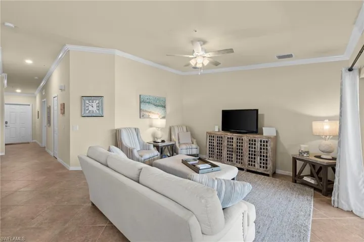 Tiled living area featuring visible vents, baseboards, crown molding, and ceiling fan
