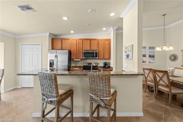 Kitchen featuring visible vents, crown molding, brown cabinets, appliances with stainless steel finishes, and a kitchen breakfast bar