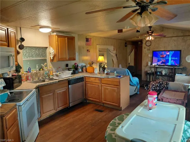 Kitchen with white stove, open floor plan, a peninsula, dark wood-style flooring, and dishwasher