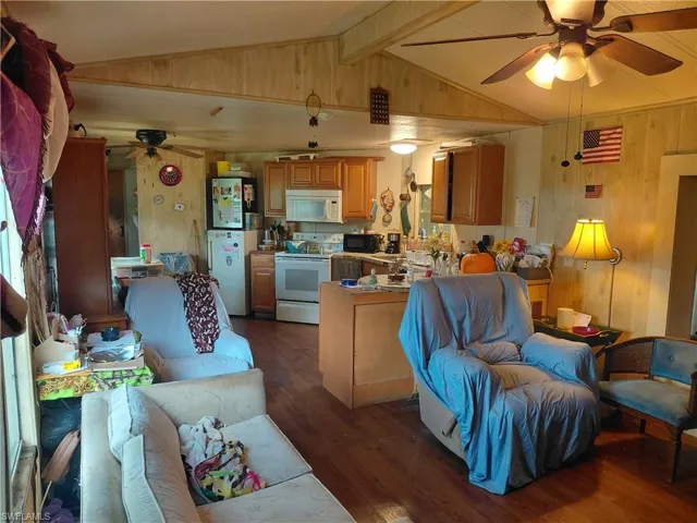 Living room with ceiling fan, dark wood-style flooring, and wood walls