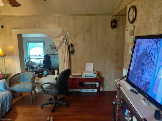 Home office with wood walls, dark wood finished floors, and a ceiling fan