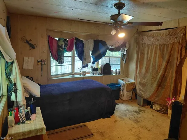 Bedroom with wooden walls, concrete floors, and a ceiling fan