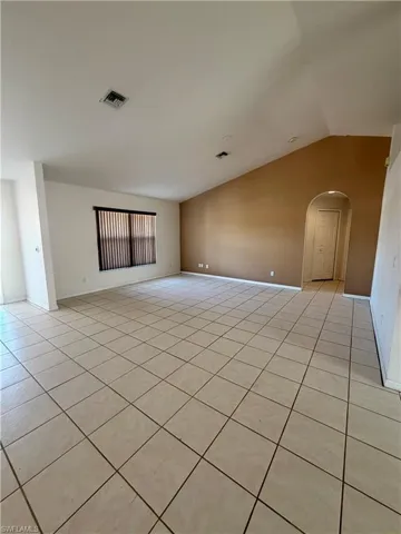 Spare room with arched walkways, light tile patterned flooring, and vaulted ceiling