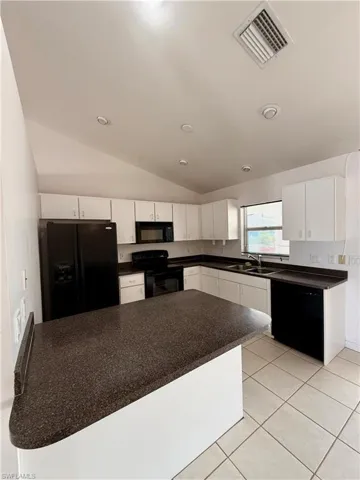 Kitchen with vaulted ceiling, black appliances, dark countertops, white cabinetry, and light tile patterned floors