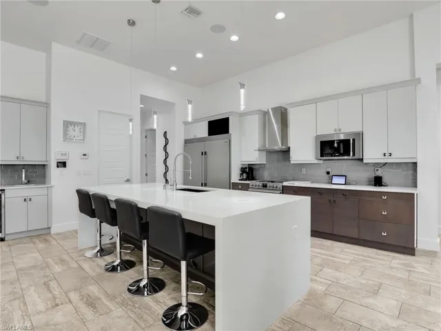 Kitchen with tasteful backsplash, white cabinets, a breakfast bar area, a kitchen island with sink, and decorative light fixtures