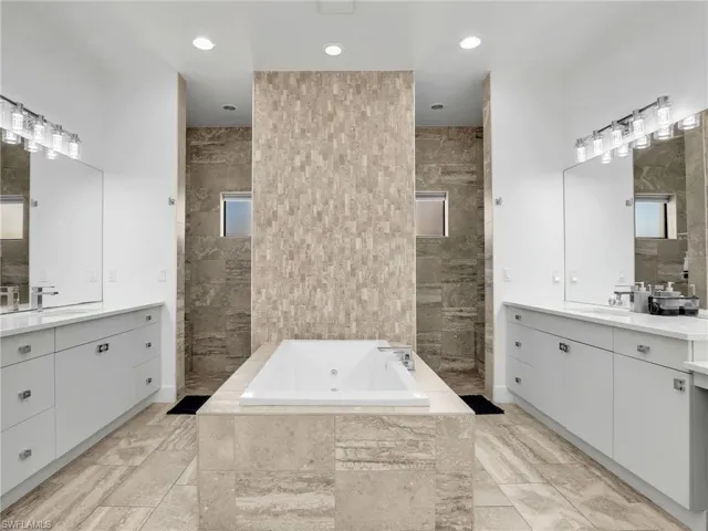 Bathroom with a whirlpool tub, two vanities, recessed lighting, and tile walls