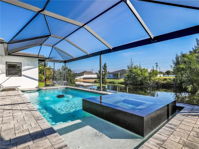View of swimming pool with a water view, glass enclosure, a sunroom, a patio, and a pool with connected hot tub