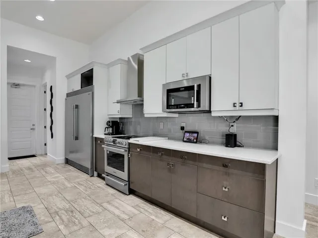 Kitchen featuring white cabinets, premium appliances, wall chimney range hood, decorative backsplash, and recessed lighting