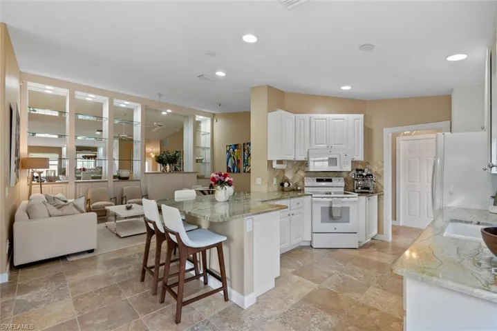 Kitchen with upgraded backsplash and granite counters, white appliances, white cabinetry, light stone countertops, and a breakfast bar