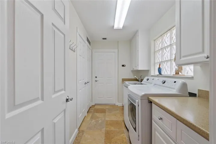Laundry area with washer and clothes dryer, stone tile floors, and cabinet space