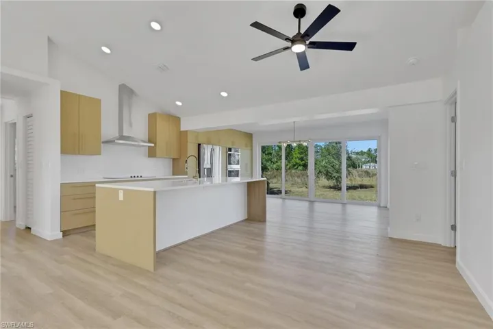 Kitchen featuring modern cabinets, wall chimney range hood, a center island with sink, light brown cabinetry, and light wood finished floors